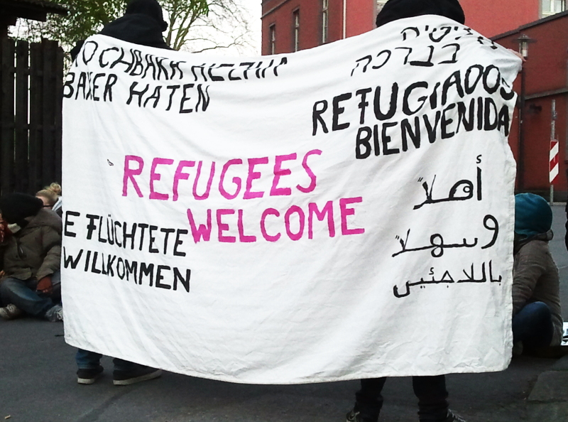 Transparent vor Flüchtlingsunterkunft. Schriftzug Flüchtlinge willkommen in verschiedenen Sprachen