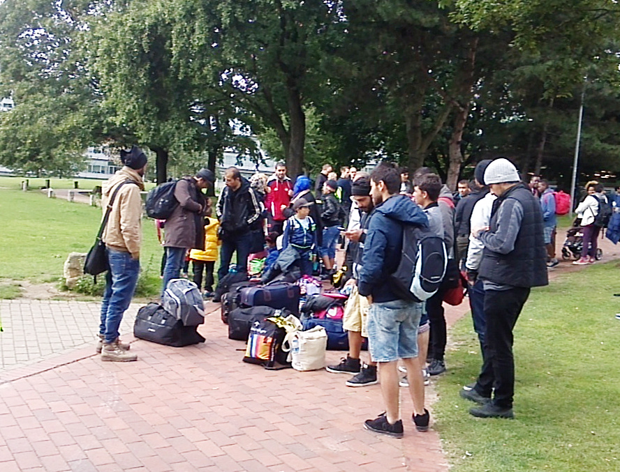 In Dortmund angekommene Geflüchtete warten mit Gepäck in einem Park