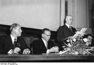 Peco Bauwens (Mitte) im Jahre 1949. Quelle: Wikipedia, Foto: „Bundesarchiv Bild 183-H26919, Bonn, Gründung Olympisches Komitee“ von Unbekannt - Dieses Bild wurde im Rahmen einer Kooperation zwischen dem Bundesarchiv und Wikimedia Deutschland aus dem Bundesarchiv für Wikimedia Commons zur Verfügung gestellt. Das Bundesarchiv gewährleistet eine authentische Bildüberlieferung nur durch die Originale (Negative und/oder Positive), bzw. die Digitalisate der Originale im Rahmen des Digitalen Bildarchivs.. Lizenziert unter Creative Commons Attribution-Share Alike 3.0-de über Wikimedia Commons - http://commons.wikimedia.org/wiki/File:Bundesarchiv_Bild_183-H26919,_Bonn,_Gr%C3%BCndung_Olympisches_Komitee.jpg#mediaviewer/File:Bundesarchiv_Bild_183-H26919,_Bonn,_Gr%C3%BCndung_Olympisches_Komitee.jpg, Lizenz: CC-BY-SA-3.0-de