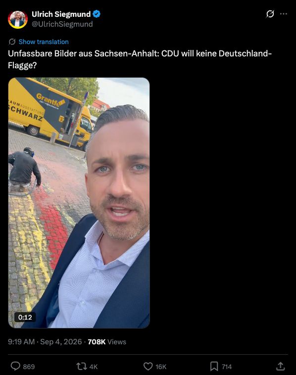 Screenshot von Ulrich Siegmunds X-Beitrag: Siegmund vor einer aufgemalten Deutschlandfahne, die mit einem Hochdruckreiniger entfernt wird.